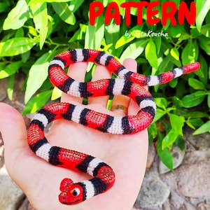 May include: A crochet snake toy featuring a repeating striped pattern of vibrant red, black, and white yarn. The snake has a textured surface and a small head with visible eyes. The text "Striped snake crochet PATTERN by TotaKsusha" is visible.