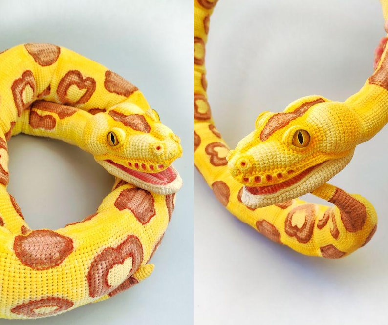 May include: A crocheted snake in yellow and brown. The snake has a detailed head with yellow eyes and a red mouth. The body is yellow with brown heart-shaped markings. The snake is coiled in a circular shape.