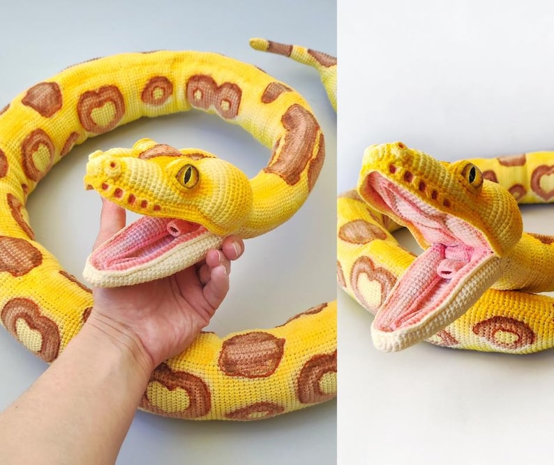 May include: A crocheted yellow snake toy with brown markings and an open mouth showing a pink interior. The snake has yellow eyes and is designed to look realistic. The toy is made of soft yarn.