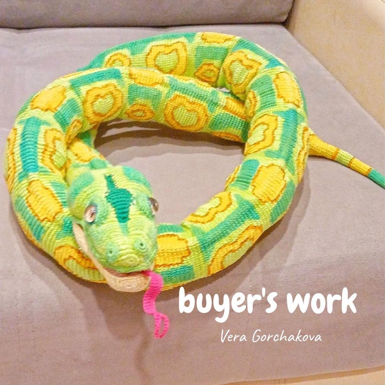 May include: A crocheted snake toy in green, yellow, and white. The snake is coiled, with a detailed head, small eyes, and a pink tongue. The text "buyer's work" and the name "Vera Gorchakova" are visible.