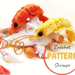 May include: Two crocheted shrimp, one orange and one yellow, rest on a white seashell with other seashells scattered around. The shrimp have black eyes and long, thin antennae. The image includes the text "Crochet PATTERN Shrimps".