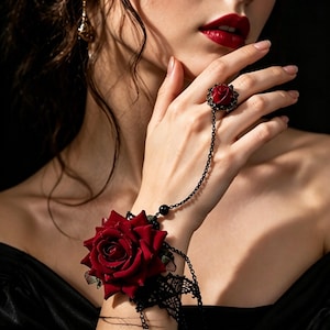 May include: A black and red rose bracelet and ring set. The bracelet features a large red rose with black lace accents. The ring has a smaller red rose design, connected to the bracelet by a delicate black chain.