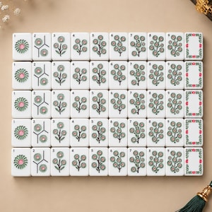 May include: A set of white rectangular mahjong tiles arranged in a grid, featuring engraved floral designs with green leaves and pink centers. Each tile displays a number from one to nine, with the final column showing a decorative floral border frame.