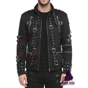 Op de afbeelding: Zwarte jas met meerdere zilveren gespen en ritsen. De jas heeft een hoge kraag en is versierd met klinknagels. De mouwen hebben extra riemen en ritsen. Onderdeel van de gothic alternatieve mode.