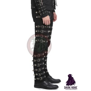 Op de afbeelding: Zwarte, kniehoge broek in gotische stijl met meerdere riemen en zilveren gespen. De broek heeft decoratieve metalen studs en wordt gecombineerd met zwarte geklede schoenen. De afbeelding bevat ook het Dark Robe-logo.