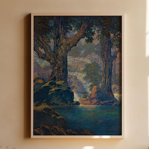 May include: A framed landscape painting depicts two large trees beside a body of water. The artwork features a muted color palette with shades of blue, green, and brown. The painting is displayed on a light-colored wall above a wooden table.