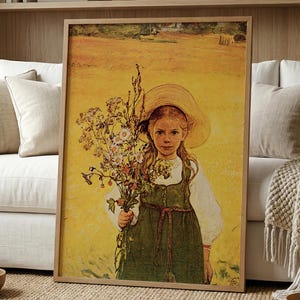 Op de afbeelding: Een ingelijste prent van een jong meisje dat wilde bloemen in een veld vasthoudt. Het meisje draagt een groene jurk en een strohoed. Het kunstwerk heeft een warm, geel kleurenpalet en is in een houten lijst geplaatst.