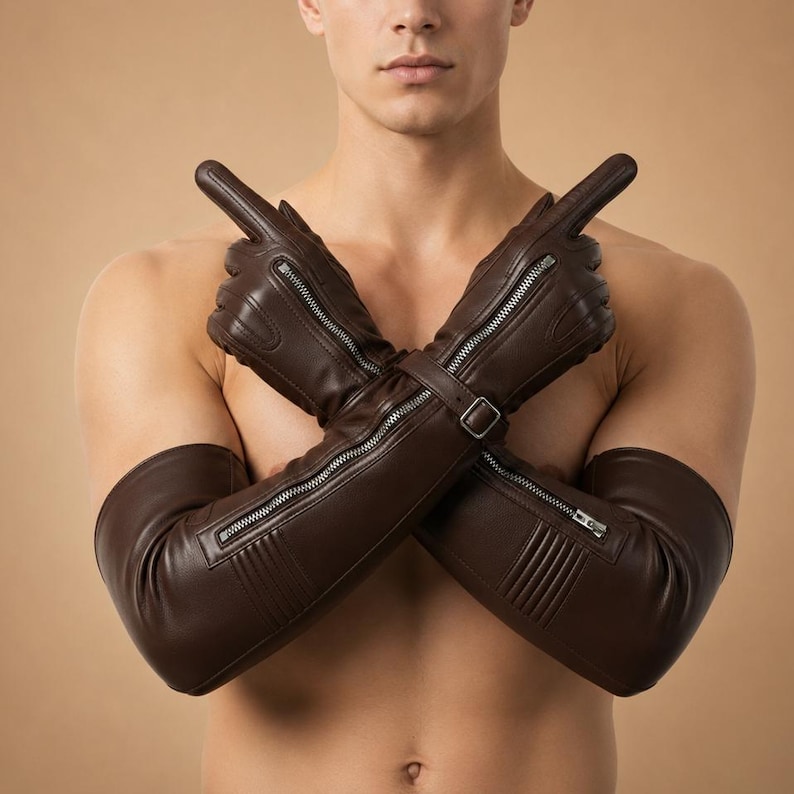 May include: Brown leather gloves with long sleeves. The gloves feature silver zippers along the length and a buckle closure at the wrist. The gloves are designed with a sleek, modern aesthetic.