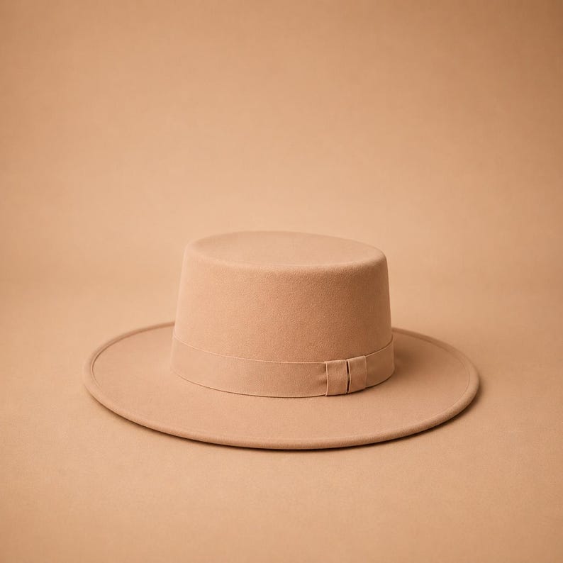 May include: A solid light tan hat with a flat crown and a wide, flat brim. The hat features a matching tonal ribbon band encircling the base of the crown, which includes a small, subtle knot detail on the side of the band for a clean finish.