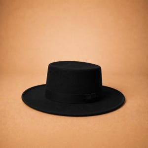 May include: A solid black hat featuring a flat crown and a wide, flat brim. The hat includes a matching black ribbon band encircling the base of the crown, providing a uniform and consistent appearance across the entire structure of the headwear.