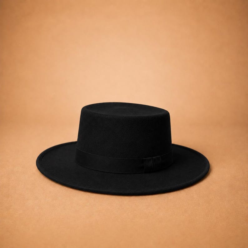 May include: A solid black hat featuring a flat crown and a wide, flat brim. The hat includes a matching black ribbon band encircling the base of the crown, providing a uniform and consistent appearance across the entire structure of the headwear.