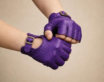 May include: Purple fingerless gloves with a textured pattern and gold-colored buckle closures. The gloves are made of a smooth material and have a wrist strap. The gloves are designed to cover the palm and fingers, leaving the knuckles exposed.