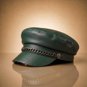 May include: A dark green leather cap with a silver chain detail across the brim. The cap has a rounded crown and a short, stiff brim. A small, decorative button is on the side of the cap.