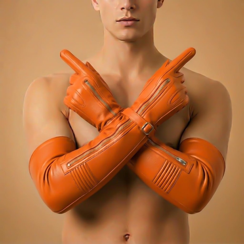 May include: Orange leather gloves with long sleeves, featuring zipper details and a buckle closure. The gloves are a vibrant shade of orange and appear to be made of a smooth leather material. The gloves are designed to cover the hands and extend up the arms.