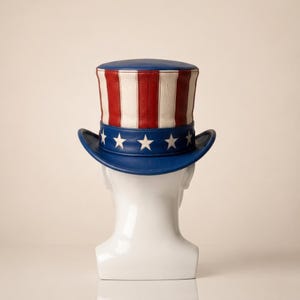 May include: A patriotic Uncle Sam hat with a blue brim and crown, featuring red and white stripes on the crown. The hat has a blue band with white stars. A classic American symbol.