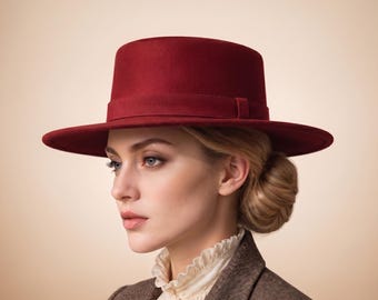 May include: A deep red felt hat with a flat crown and a wide, structured brim. The hat features a matching red ribbon band encircling the base of the crown. The material has a smooth, uniform texture, and the design maintains a clean, symmetrical shape.