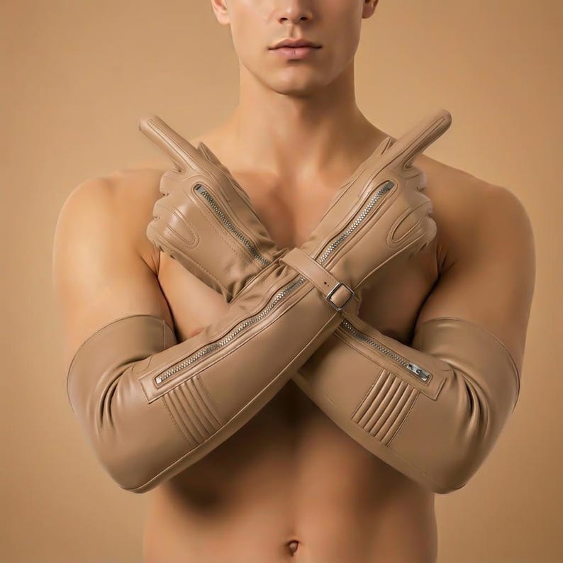 May include: Tan leather gloves with long sleeves and silver zippers. The gloves have a buckle closure at the wrist and are designed with vertical lines on the forearm. The gloves are a neutral color and appear to be made of a soft material.