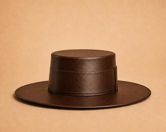 May include: A dark brown flat-brimmed hat with a structured cylindrical crown and a wide, circular brim. The hat features a smooth, uniform texture and a matching dark brown band wrapped around the base of the crown, creating a clean silhouette.