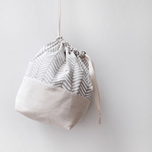 Puede incluir: Una bolsa de cord&oacute;n de color gris y blanco con un fondo beige. La bolsa est&aacute; colgada de una cuerda blanca.