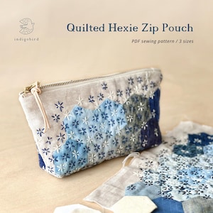 May include: A quilted zip pouch featuring a hexagonal patchwork design in shades of blue and white with embroidered star details. The text Quilted Hexie Zip Pouch and PDF sewing pattern / 3 sizes is visible along with the indigobird logo.