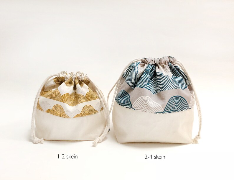 Puede incluir: Dos bolsas de cord&oacute;n hechas de tela blanca con una parte superior estampada. La bolsa m&aacute;s peque&ntilde;a tiene un estampado dorado y blanco y la bolsa m&aacute;s grande tiene un estampado azul y blanco. Las bolsas est&aacute;n etiquetadas como "1-2 ovillos" y "2-4 ovillos".