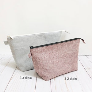 May include: Two fabric pouches in light gray and mauve. The gray pouch has a white zipper and the text "2-3 skein". The mauve pouch has a black zipper and the text "1-2 skein". Both pouches are rectangular with a trapezoidal shape.
