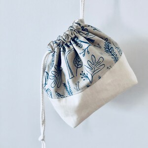 May include: A small, white drawstring bag with a blue and white floral print. The bag is made of cotton and has a simple design.