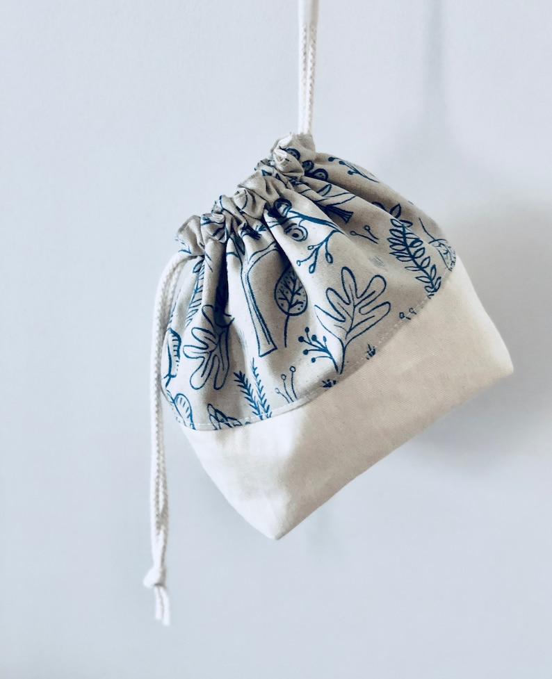 May include: A small, white drawstring bag with a blue and white floral print. The bag is made of cotton and has a simple design.
