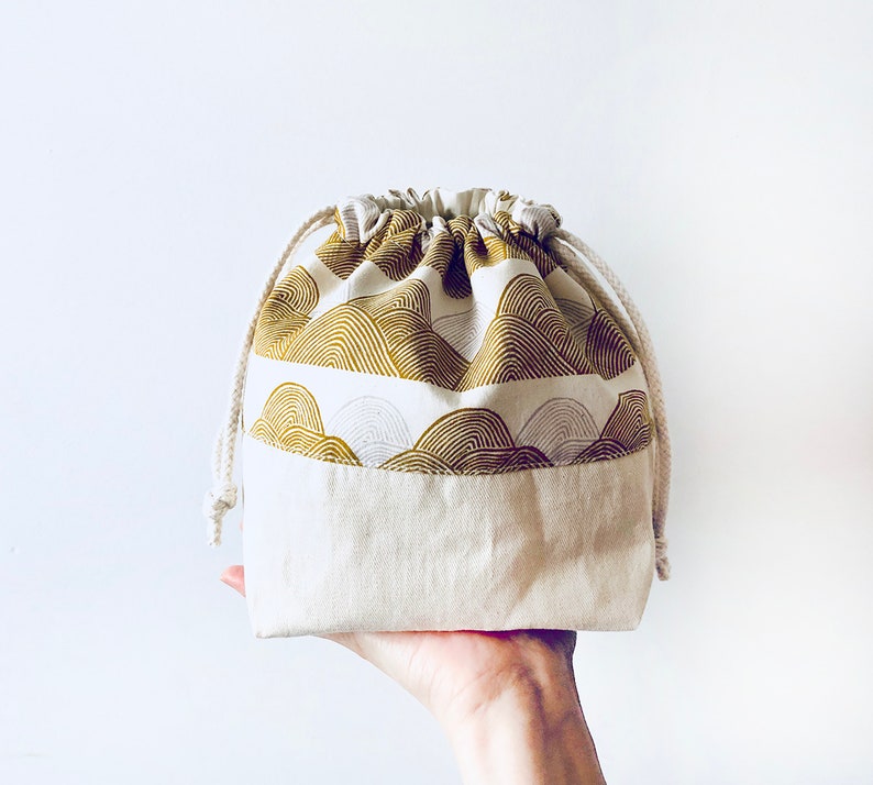 May include: A white drawstring bag with a gold and white patterned fabric lining. The bag is made of a soft, natural fabric and has a simple, elegant design.