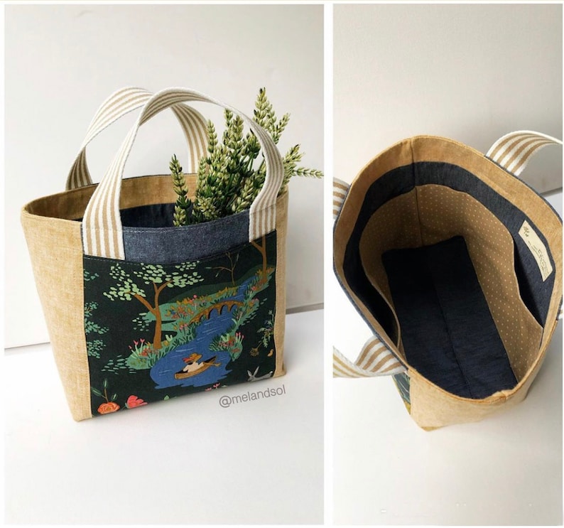 May include: A beige tote bag with a white and brown striped handle. The bag is lined with a dark blue fabric with white polka dots. The exterior of the bag features a colourful fabric with a nature scene.