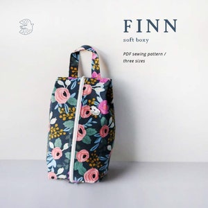 Könnte beinhalten: Eine Reißverschlusstasche mit Blumendruck und einem oberen Tragegriff. Die Tasche ist marineblau mit rosa, gelben und grünen Blumen. Der Text "FINN soft boxy PDF sewing pattern / three sizes" ist auf weißem Hintergrund gedruckt.