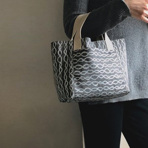 May include: A grey tote bag with a white chain-like pattern. The bag has cream-coloured straps.