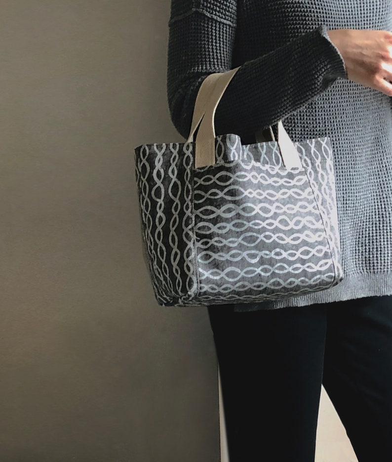 May include: A grey tote bag with a white chain-like pattern. The bag has cream-coloured straps.