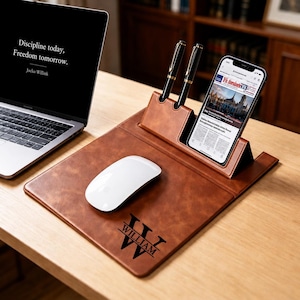 May include: A brown leather desk organizer mat featuring a white computer mouse, two black pens in upright holders, and a smartphone stand. The mat is personalized with the black text "WILLIAM" centered within a large stylized letter "W".