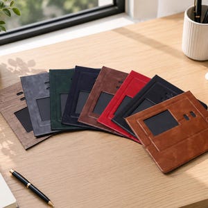 May include: A collection of rectangular passport holders arranged in a fan shape, featuring various colors including brown, gray, green, dark blue, reddish-brown, red, and black. Each holder has a clear rectangular window and two small oval cutouts.
