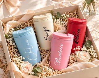 Può includere: Una confezione regalo contenente quattro bicchieri termici in azzurro, crema, rosa e rosso. Ogni bicchiere è dotato di coperchio e di un nome personalizzato in corsivo: Chloe, Sage, Beatrice e Rebecca. La scatola è riempita con fiori e decorazioni.