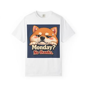 以下が含まれることがあります： 不機嫌そうな表情の漫画の柴犬が描かれた白いTシャツ。犬は茶色と白で、汗のしずくがあります。「Monday? No thanks.」というテキストが犬の下にあります。