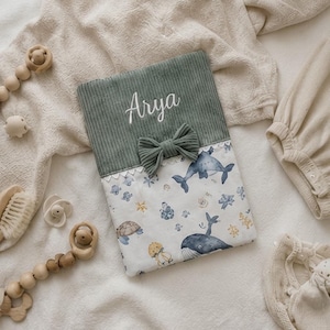 Peut inclure: Une housse en tissu rectangulaire avec une partie supérieure en velours côtelé vert sauge brodée du prénom Arya en blanc, un nœud assorti et une partie inférieure blanche imprimée de baleines bleues, de tortues et de coraux jaunes.