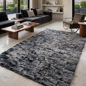 Puede incluir: Salón moderno con una gran alfombra gris de piel sintética. La alfombra es el punto focal, con una apariencia texturizada. Sofás grises oscuros, mesas de centro de madera y un sillón de terciopelo completan el diseño contemporáneo. La habitación tiene grandes ventanales y paredes neutras.