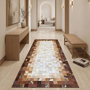 May include: A hallway featuring a rectangular cowhide rug with a patchwork design in shades of brown, tan, and white. The hallway has light-coloured walls, wooden doors, and a bench. A painting and a console table are on the left.