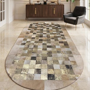 Könnte beinhalten: Ovaler Teppich mit Patchwork-Design. Der Teppich hat Quadrate in Beige, Braun, Gold und Schwarz. Der Teppich liegt in einem Flur mit einem Holzschrank und einem Spiegel. Die Maße des Teppichs sind in Zentimetern.