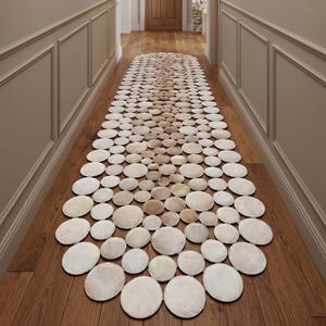 May include: A hallway featuring a wooden floor and a rug composed of circular, pale stones. The walls are painted in a neutral tone and decorated with framed botanical prints. Recessed lights illuminate the space, with a wooden door at the end.