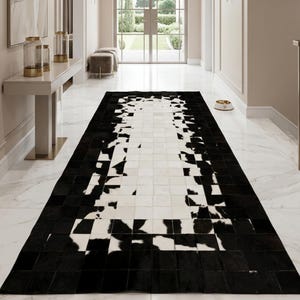 May include: A black and white cowhide rug with a geometric pattern in a hallway. The rug's design features a mix of black and white squares, creating a striking visual contrast. The hallway has white marble flooring and neutral-toned walls.
