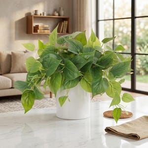 Pode incluir: Uma exuberante planta pothos artificial com folhas verdes vibrantes em forma de coração que caem de um vaso de cerâmica cilíndrico branco, simples e liso. A planta é exibida como centro de mesa com folhagem densa e variada.