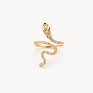 Könnte beinhalten: Ein goldfarbener Schlangenring mit gewundenem Design. Der Schlangenkopf ist erhoben, und der Körper windet sich um den Finger. Der Ring ist mit kleinen, klaren Edelsteinen besetzt, die dem Schmuck Glanz und Details verleihen.