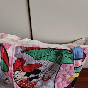Może przedstawiać: Pikowana torba typu tote z nadrukiem Myszki Minnie. Torba ma r&oacute;żową, czerwoną i białą kolorystykę z rombowym wzorem. Uchwyty są niebieskie. Torba jest wykonana z tkaniny i jest przeznaczona do przenoszenia przedmiot&oacute;w.