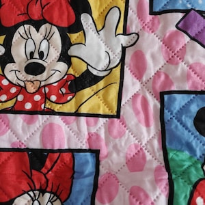 Może przedstawiać: Pikowana tkanina z Minnie Mouse w r&oacute;żnych pozach. Projekt zawiera kwadraty z wizerunkami Minnie Mouse na r&oacute;żowym tle z dużymi r&oacute;żowymi kropkami. Obrazy są obramowane ż&oacute;łtymi, niebieskimi i fioletowymi obw&oacute;dkami.