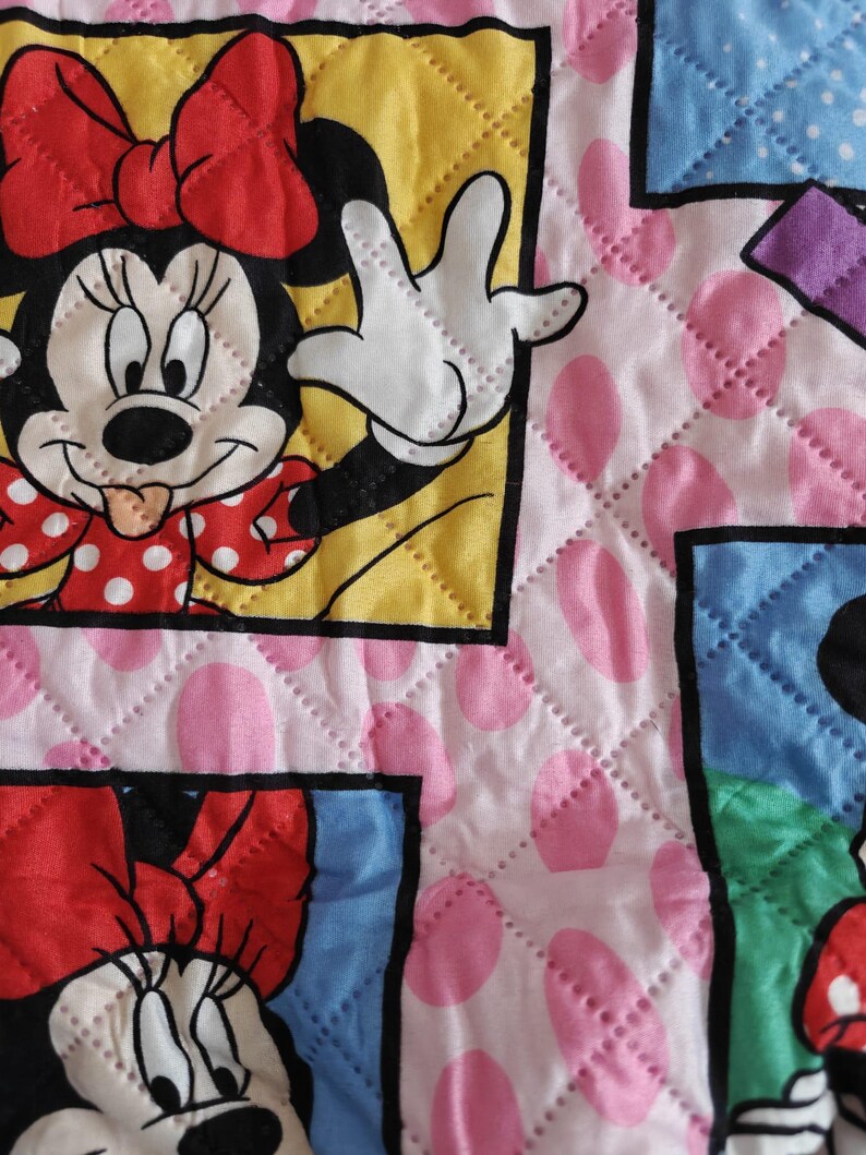 Może przedstawiać: Pikowana tkanina z Minnie Mouse w r&oacute;żnych pozach. Projekt zawiera kwadraty z wizerunkami Minnie Mouse na r&oacute;żowym tle z dużymi r&oacute;żowymi kropkami. Obrazy są obramowane ż&oacute;łtymi, niebieskimi i fioletowymi obw&oacute;dkami.