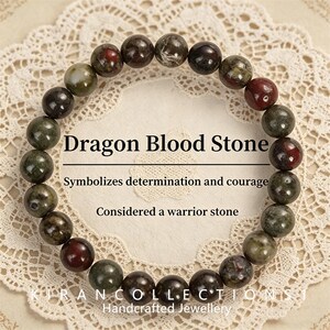 May include: A Dragon Blood Stone bracelet with round beads in green, brown, and red hues. The image includes text stating "Dragon Blood Stone" and "Symbolizes determination and courage".