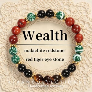 May include: A bracelet with red, green, black, and brown beads. The bracelet includes malachite, redstone, and red tiger eye stones. The word "Wealth" is displayed in large black letters. Gold-coloured beads separate the stones.